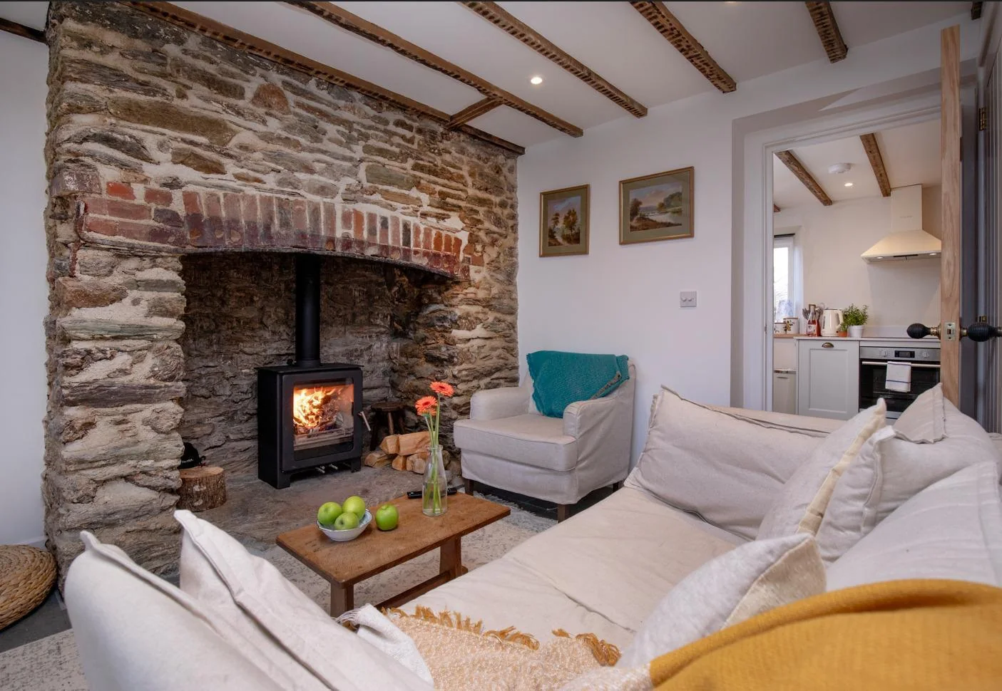 Living room showing the original stone fireplace, wood burner and kitchen beyond